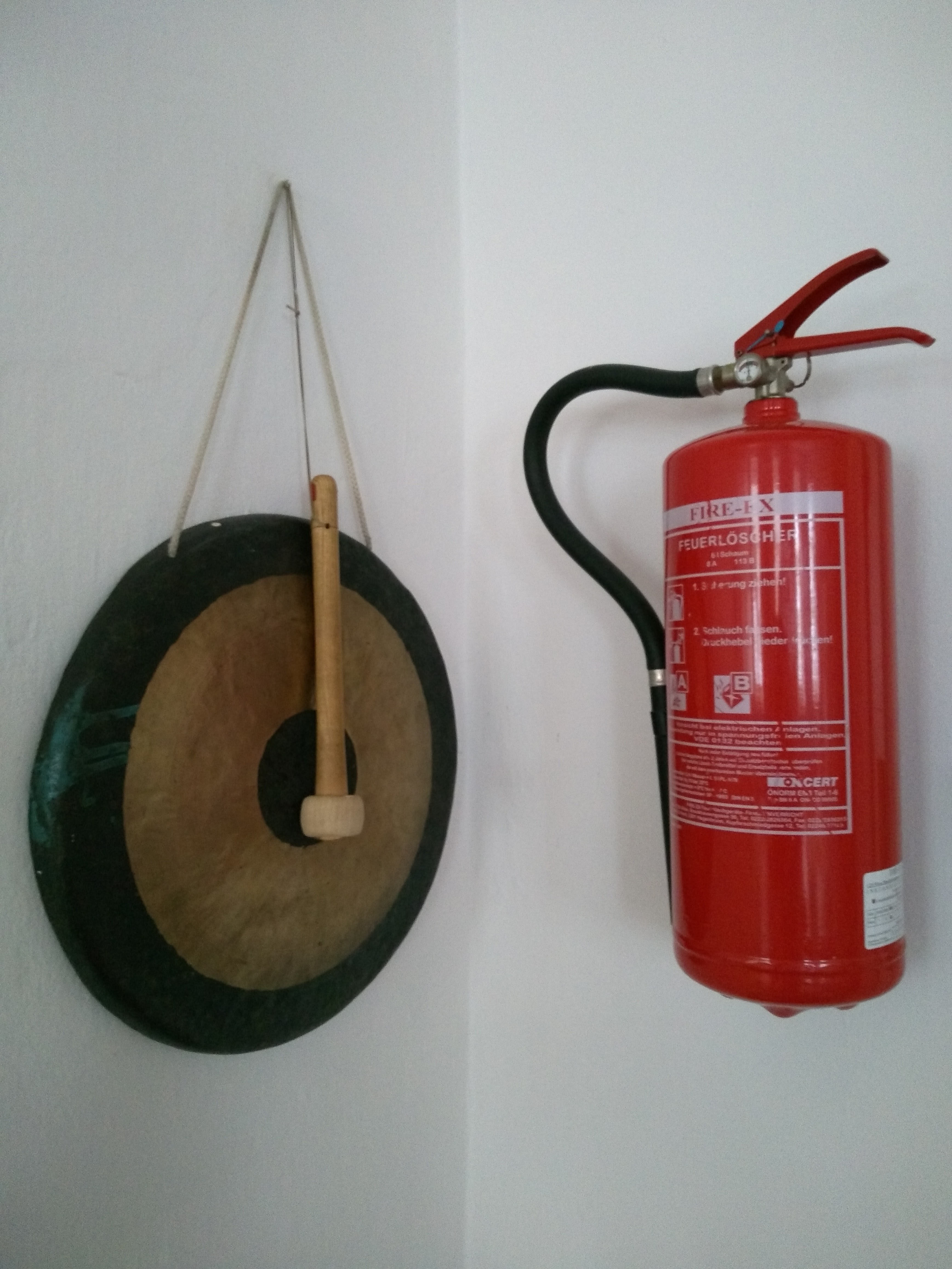 Das Bild zeigt einen Feuerlöscher und einen Gong, die nebeneinander an einer Wand montiert sind.